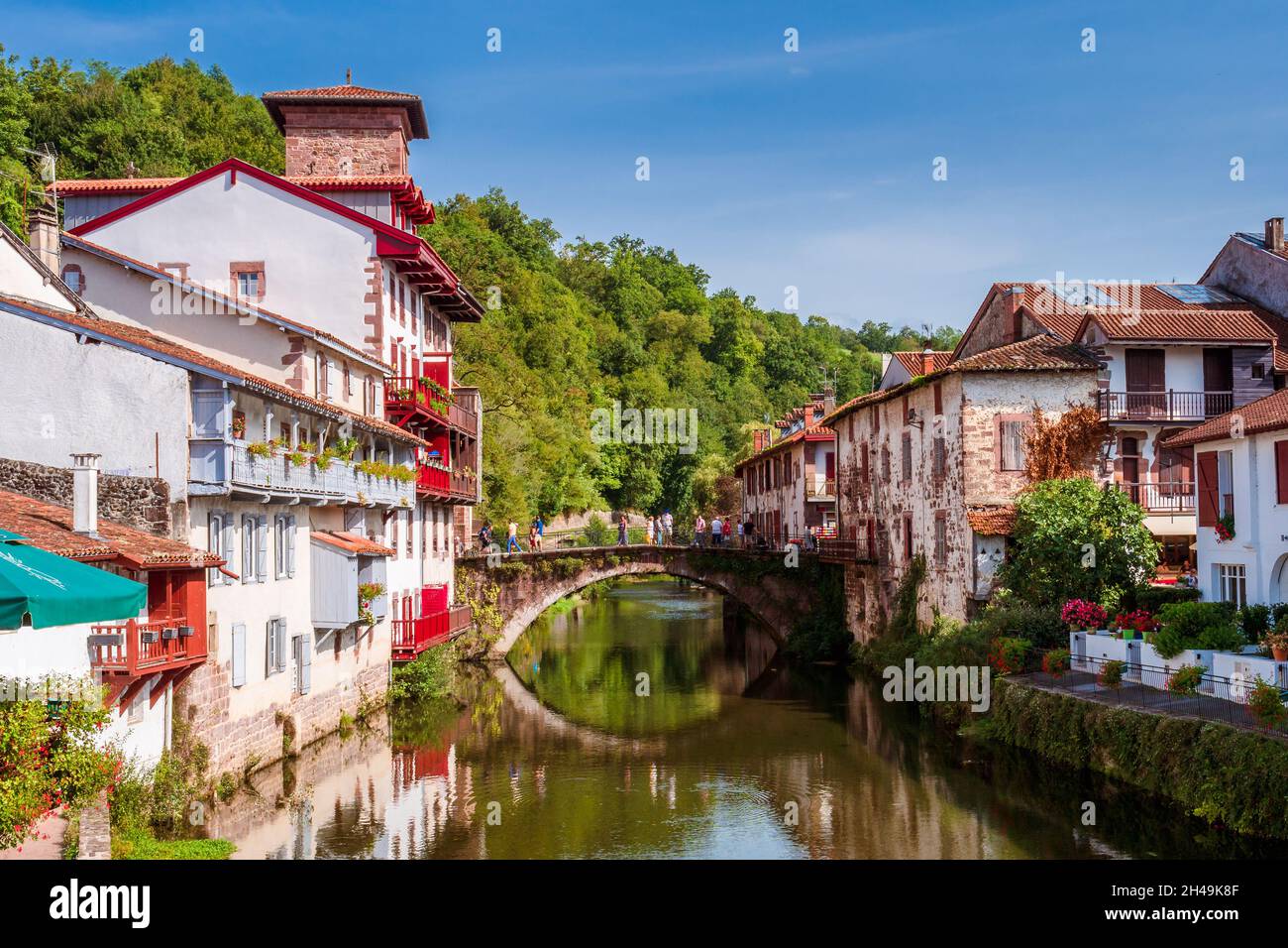 Panoramic view of French white town with red balconies and flowers crossed by a tranquil river. Saint-Jean-Pied-de-Port, France Stock Photo