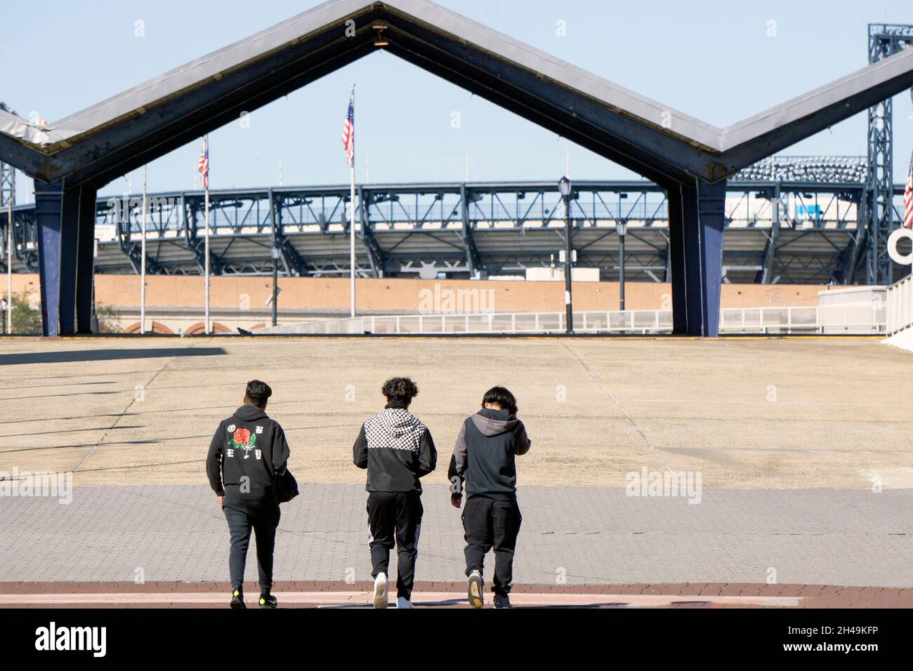 Three young men walk on a ramp taking them from Flushing Meadows Corona Park to Citi Field and the number 7 subway train. In Queens, New York City. Stock Photo