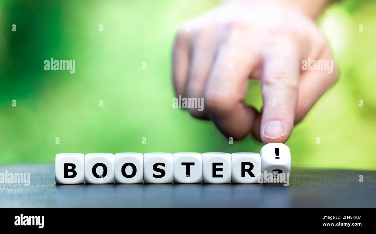 Symbol for a covid booster shot. Hand turns dice and changes the expression 'booster?' to 'booster!'. Stock Photo