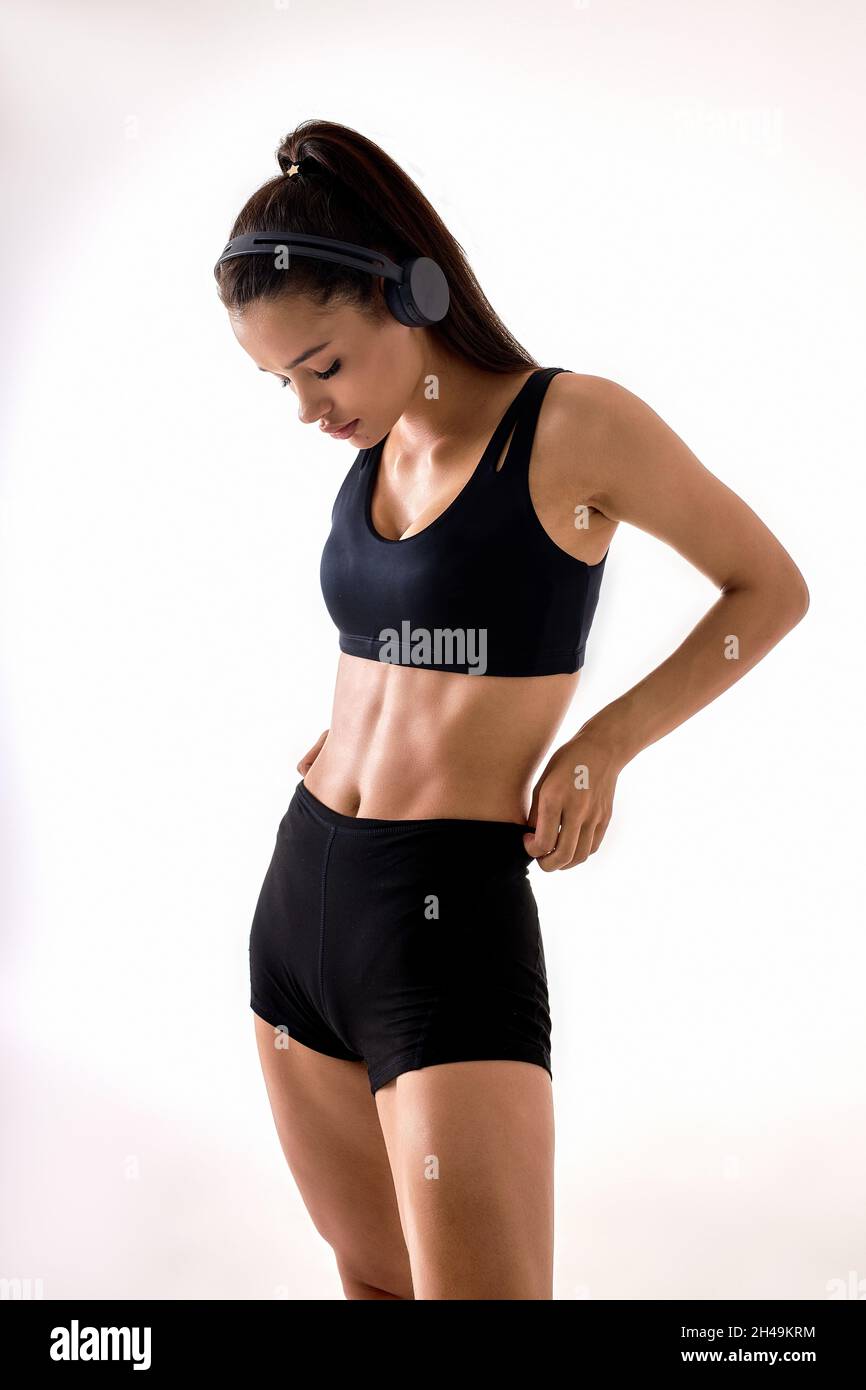 Beautiful attractive brunette woman wearing black sportswear and headphones  posing at camera, working out training looking at abs muscles, hair in pon  Stock Photo - Alamy
