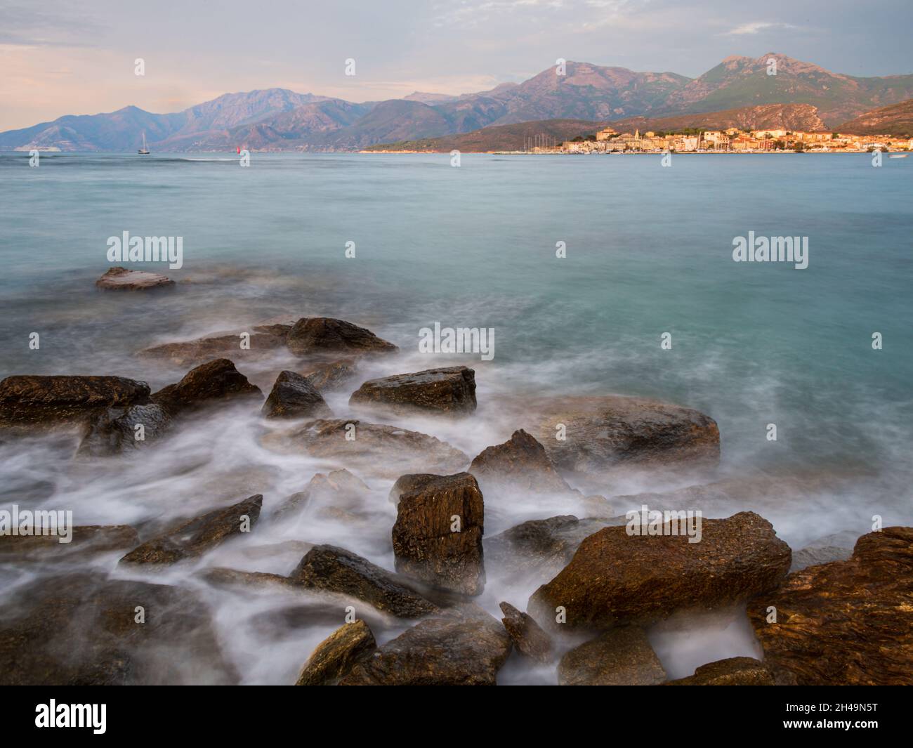 seascape of rocks going into the méditerranéen sea with the town of Saint Florent , Corsica , France in the distance . holiday destinations . Stock Photo