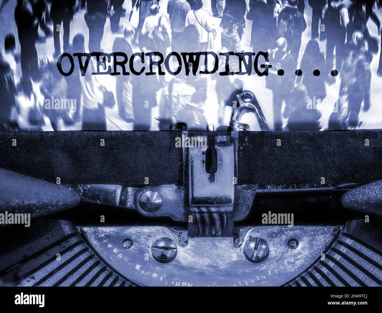 Typewriter displaying the words Overcrowding with a crowd of people in the background in a mono blue tone Stock Photo