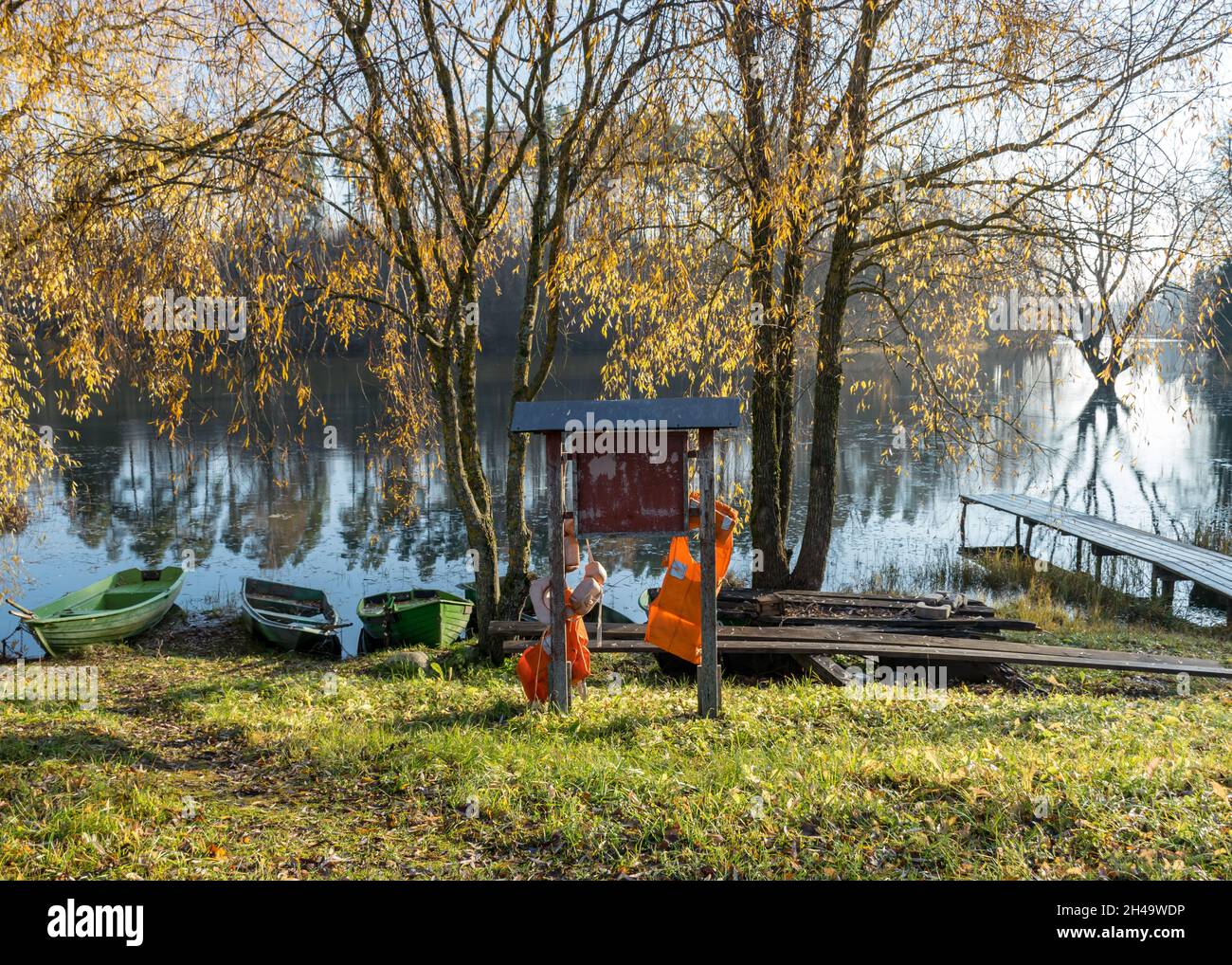 bright autumn landscape with lake shore, yellow birch branches, boats and information board with bright life jackets, fishing concept Stock Photo