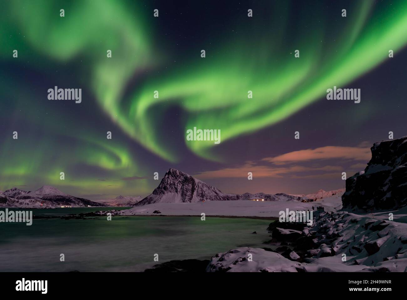 Aurora Borealis in the Lofoten Islands, Norway. Northern lights dancing on the sky. Snowy mountains and the sea coast Stock Photo