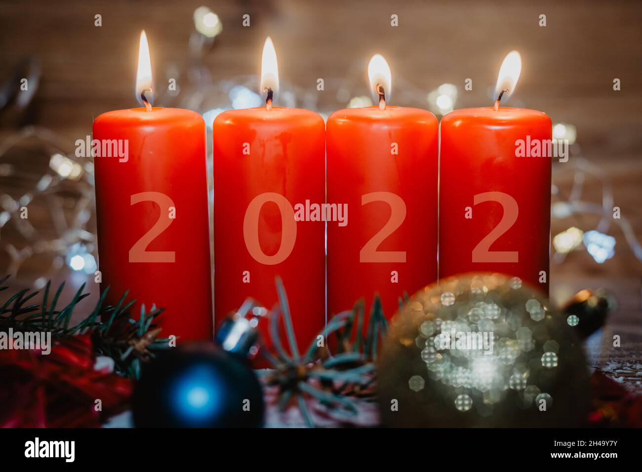Four red Advent candles with 2022 figures on them and Christmas decorations lying in the snow as a template Stock Photo