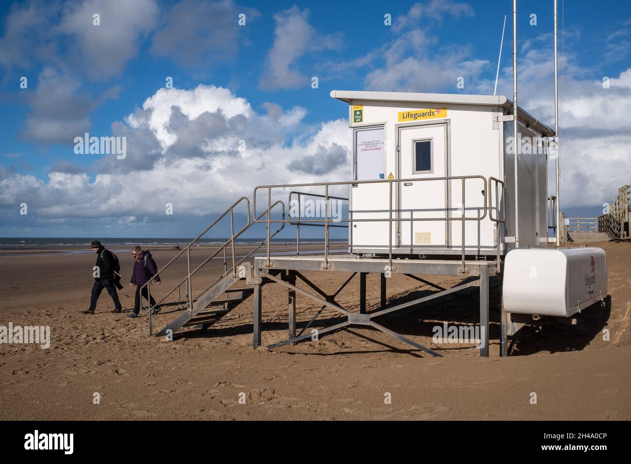 Lifeguards hut on the beach with 2 people walking past wearing winter coats Stock Photo
