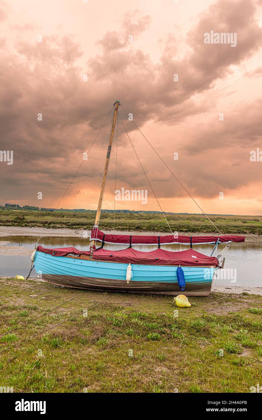 A sailing dinghy beside the River Glaven on the salt marshes at Blakeney National Nature Reserve at Blakeney, Norfolk UK Stock Photo
