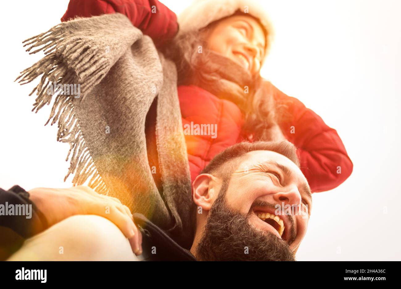 Happy couple of travelers in love enjoying winter time outdoor - Handsome hipster man with young woman on piggyback balance - Relationship concept Stock Photo