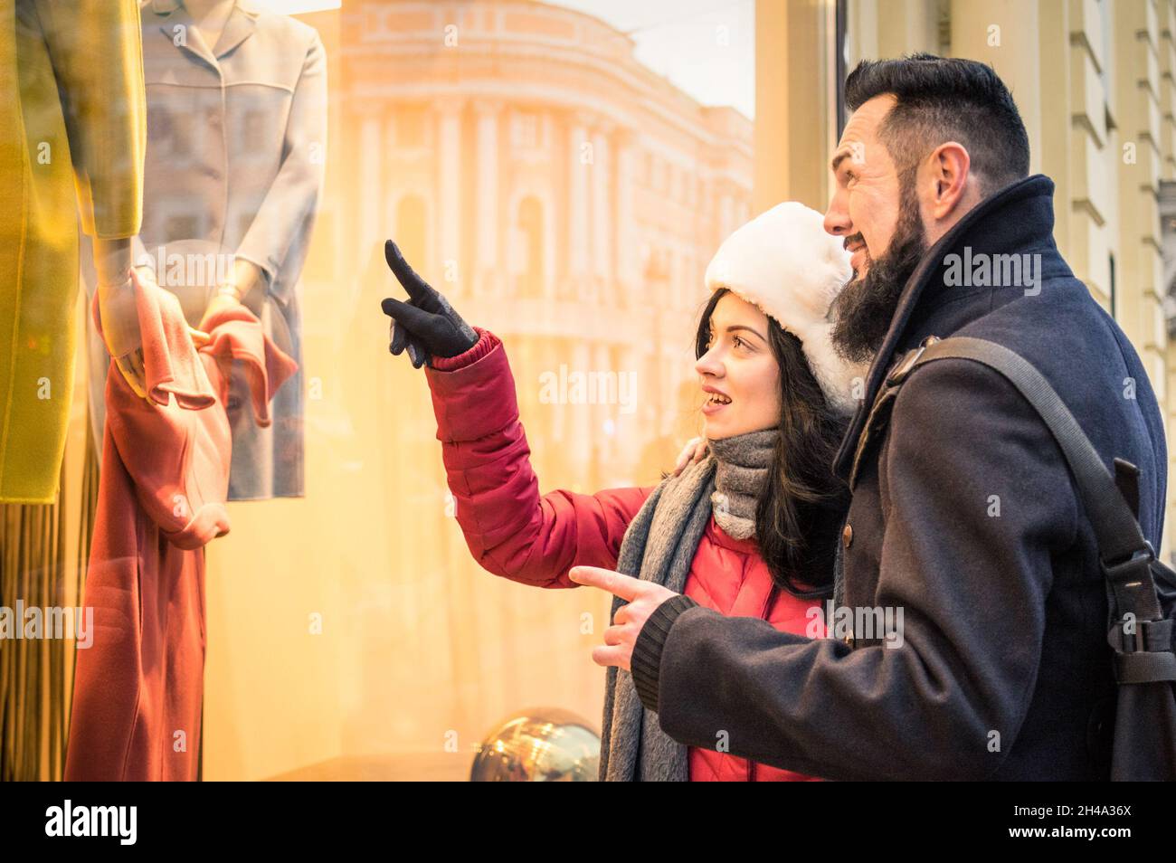 Modern hipster couple shopping on winter cloth pointing moda store window display - Consumerism concept with young fashion people Stock Photo