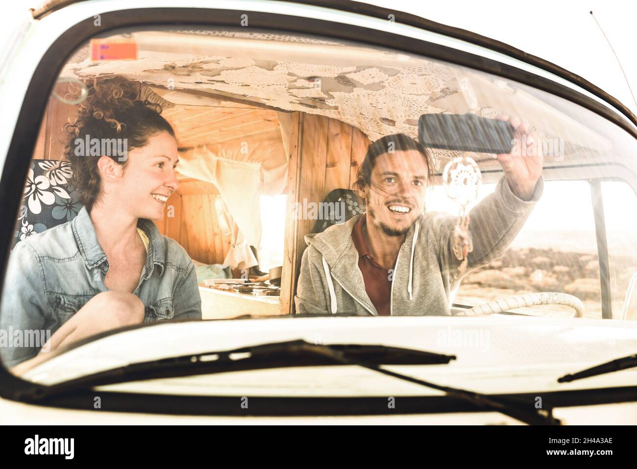 Indie couple ready for roadtrip on oldtimer mini van transport - Travel lifestyle concept with young hippie people having fun traveling on minivan Stock Photo