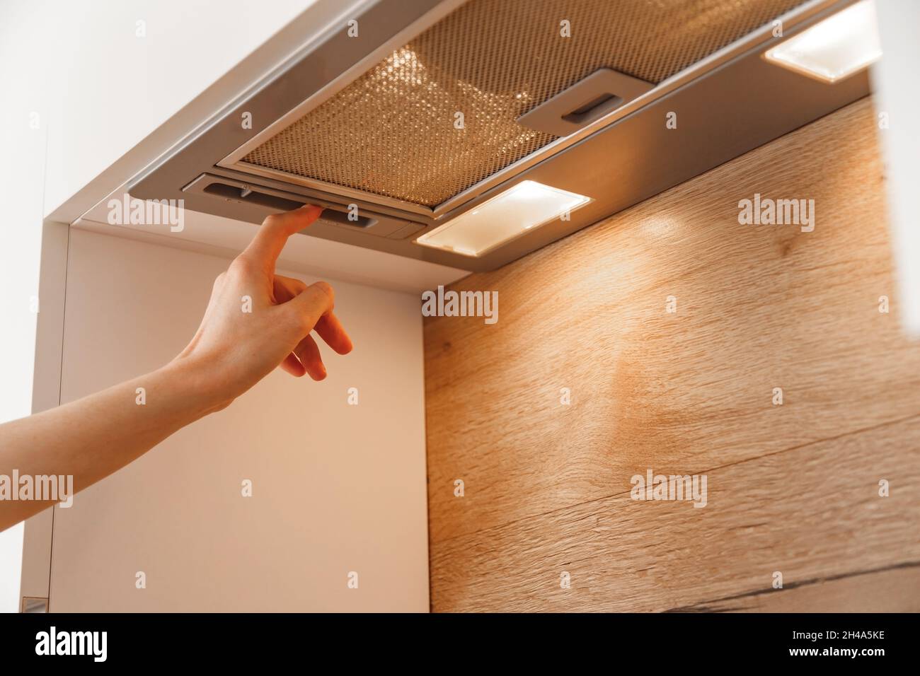 Woman hand turn on embedded cooker hood in white modern kitchen Stock Photo