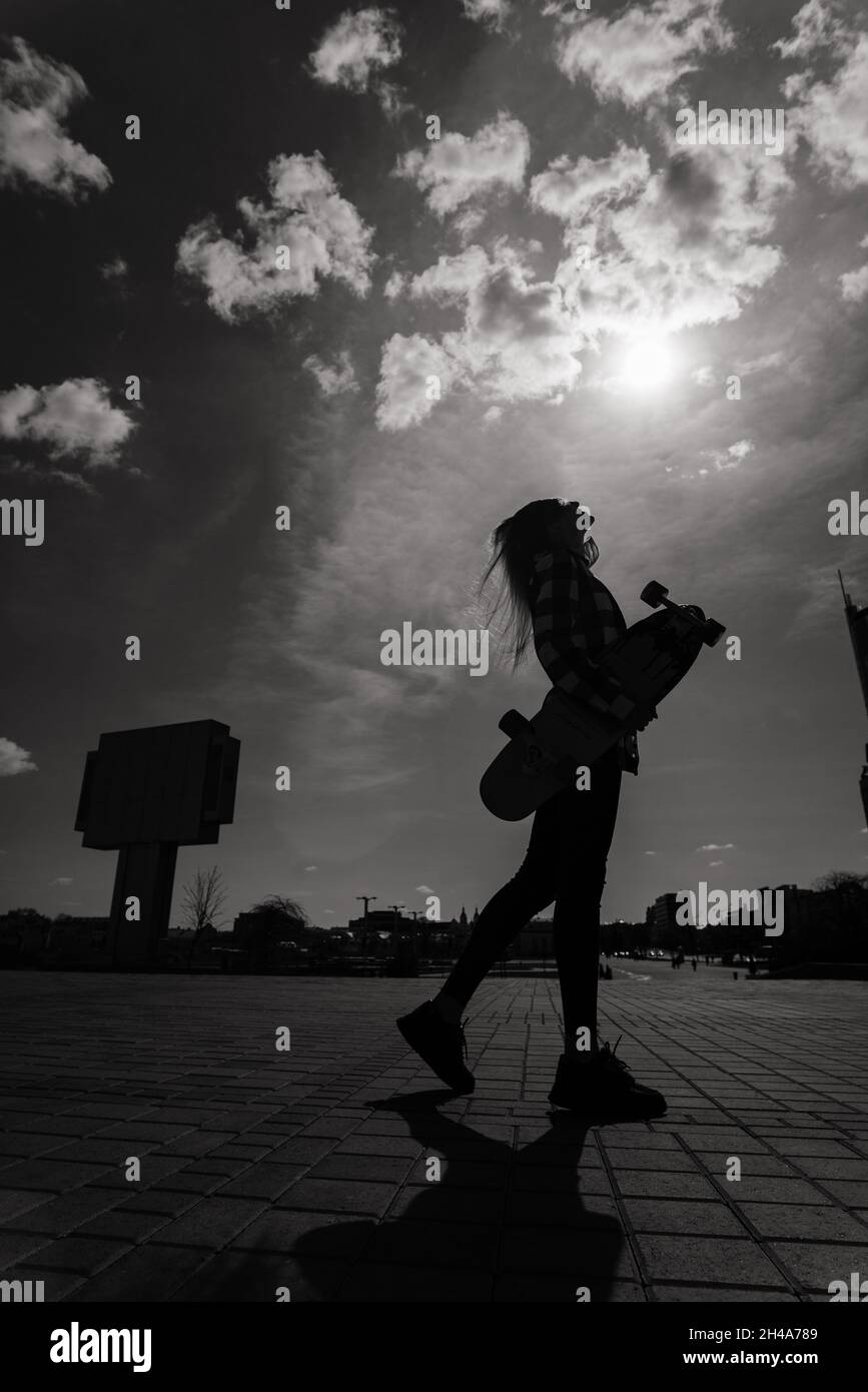 Beautiful young skater woman riding on her longboard in a city. Stock Photo