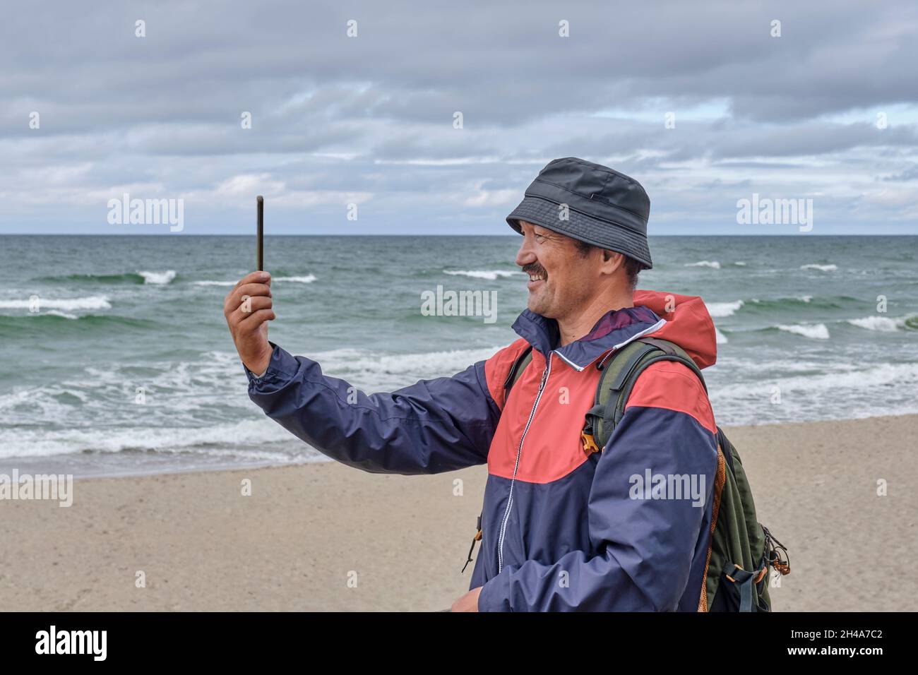 Senior asian man with backpack on seashore talking via video communication. Stock Photo