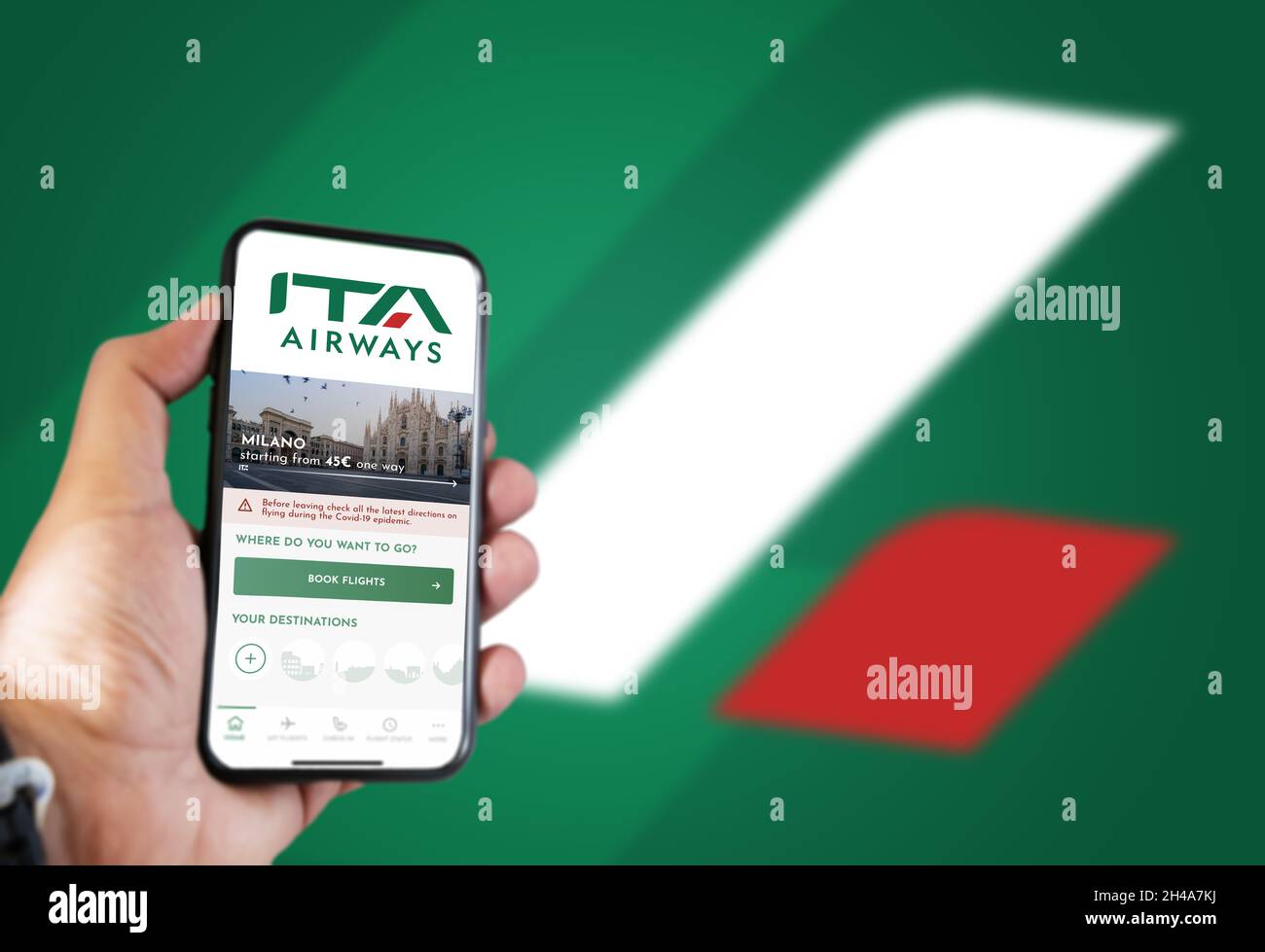 Rome, IT, October 2021: hand holding a phone with the ITA Airways app on the screen and the logo blurred on a green background.ITA Airways is the new Stock Photo