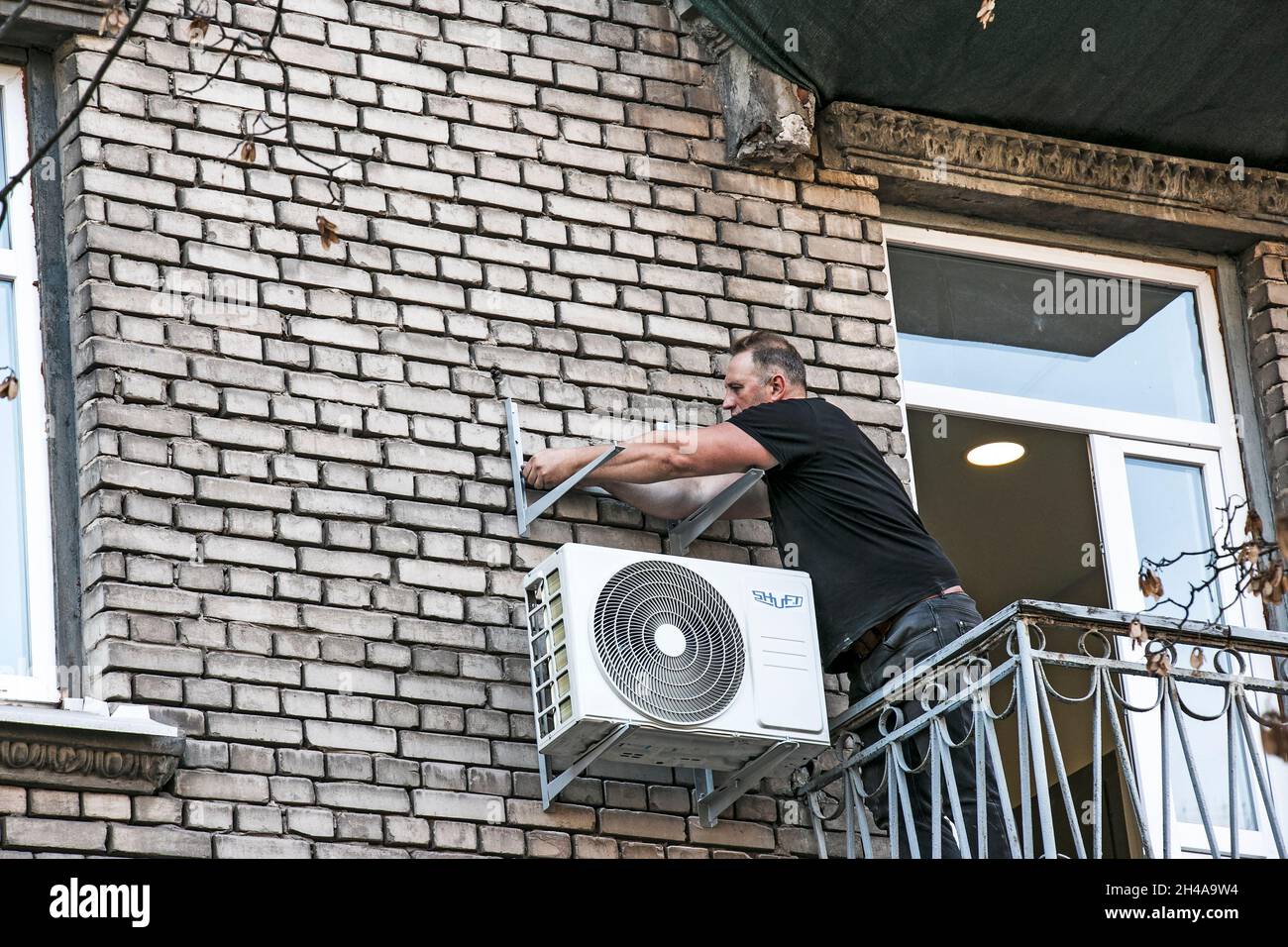 Dnepropetrovsk, Ukraine - 10.22.2021: A worker installs the bracket for the outdoor unit of the air conditioner on the wall of the house. Stock Photo