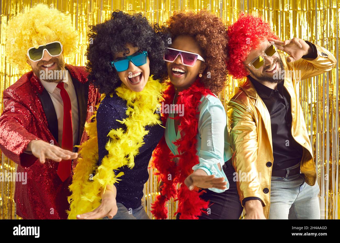 Group of happy people in boas and curly wigs dancing and having fun at disco party Stock Photo