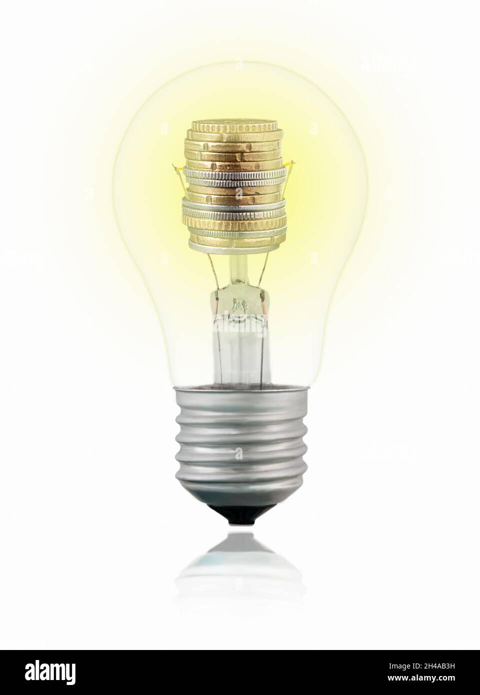 Isolated transparent tungsten light bulb with coins inside on white background with reflection. Concept of green energy and energy saving Stock Photo
