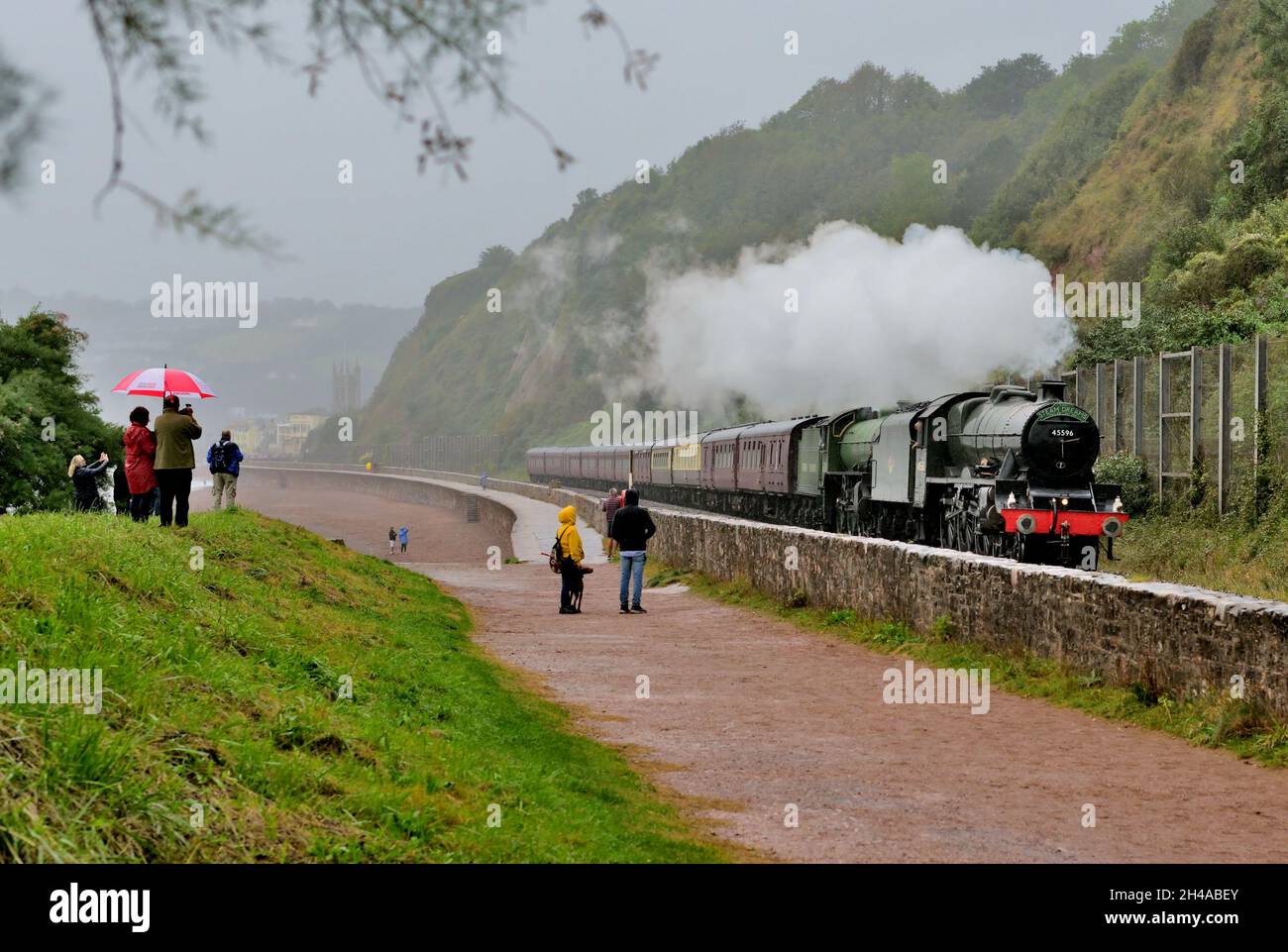 Steam train in the rain. Enthusiasts brave the inclement weather to watch The Mayflower rail-tour passing Sprey Point at Teignmouth, South Devon. Stock Photo