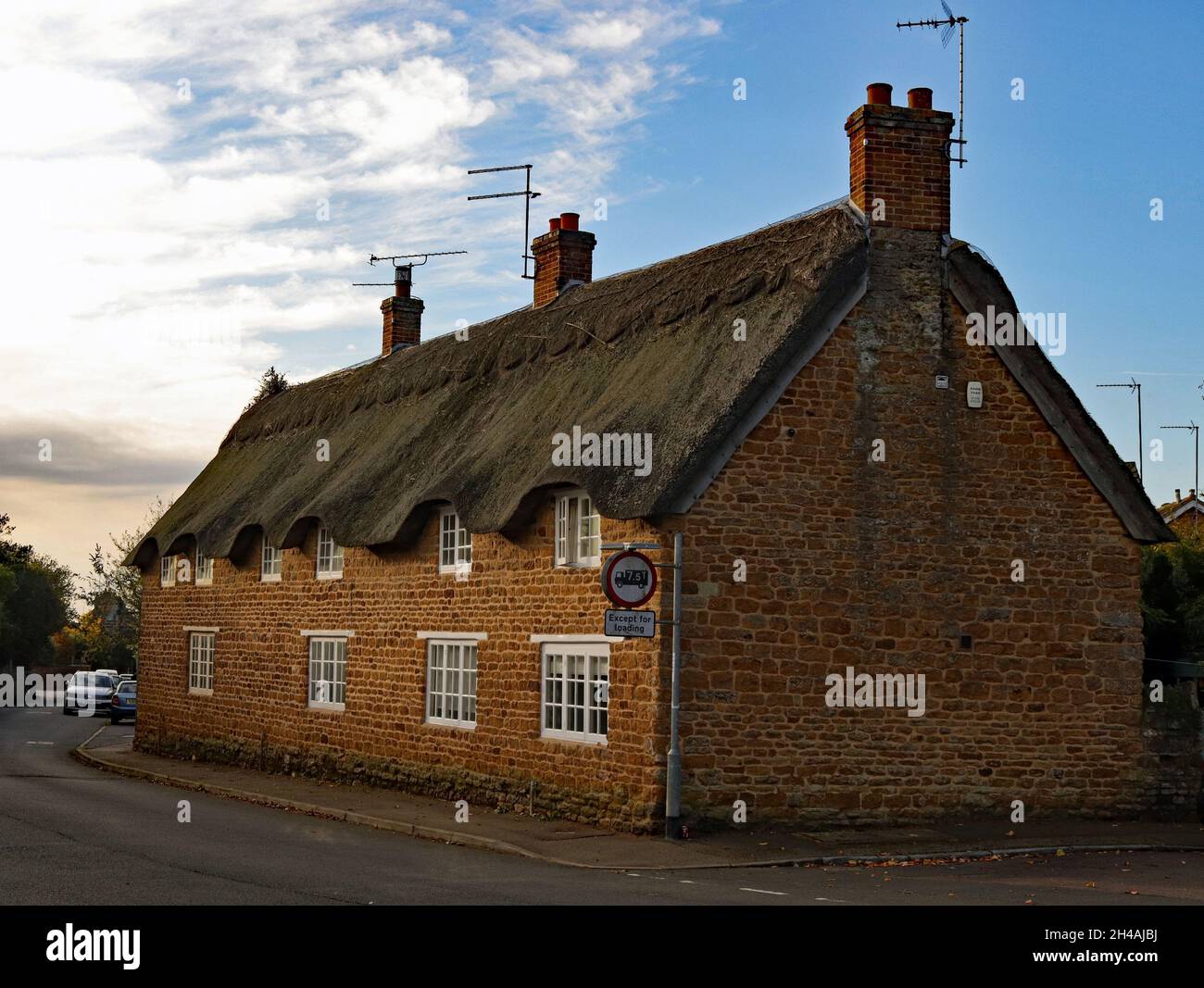 Thatched cottages on the High Street in Ecton, the Northamptonshire ironstone building stones are warmed by the morning sun. Stock Photo