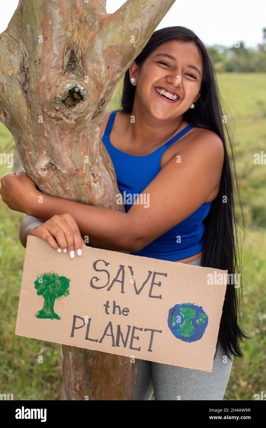 Vertical photo of woman asking to save the planet. Young latin adult woman holds sign asking to save the planet in a tropical location. Save Earth Stock Photo