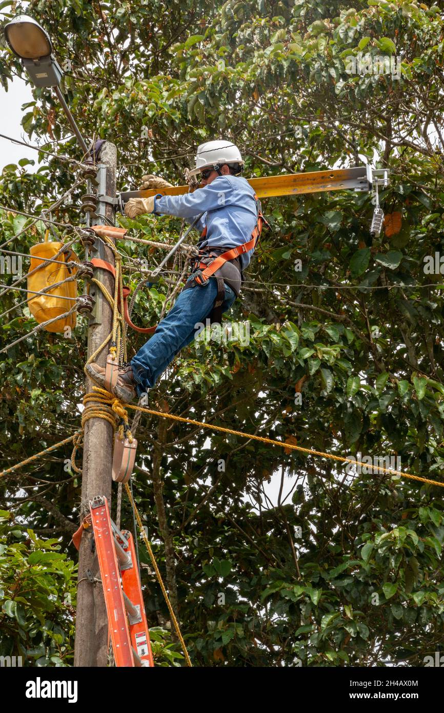 Electrician working at heights, maintenance and repair of high voltage electrical cables. Electrician using safety equipment, full body harness. Stock Photo