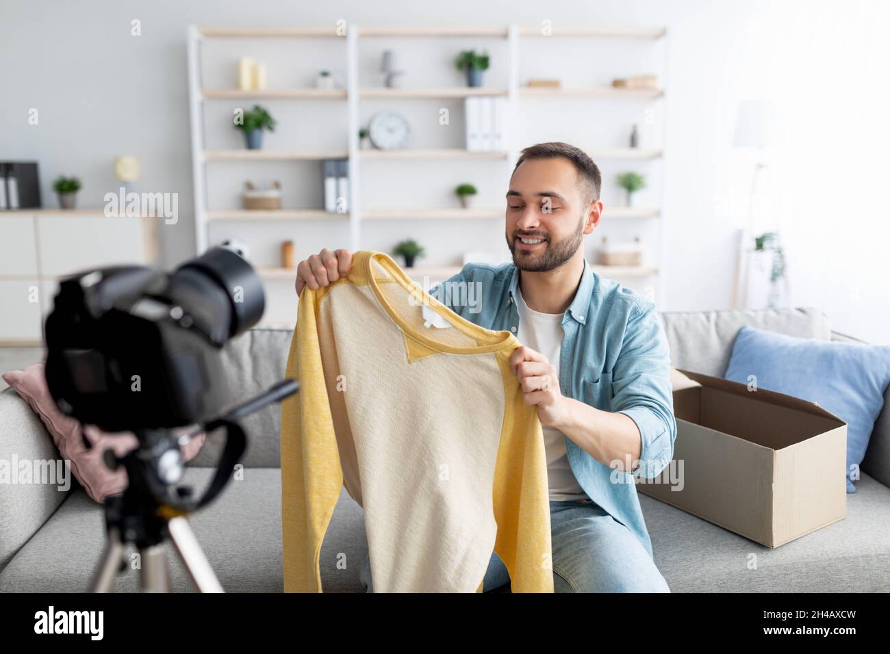 Fashion blogger recording video content, unboxing new sweater at home