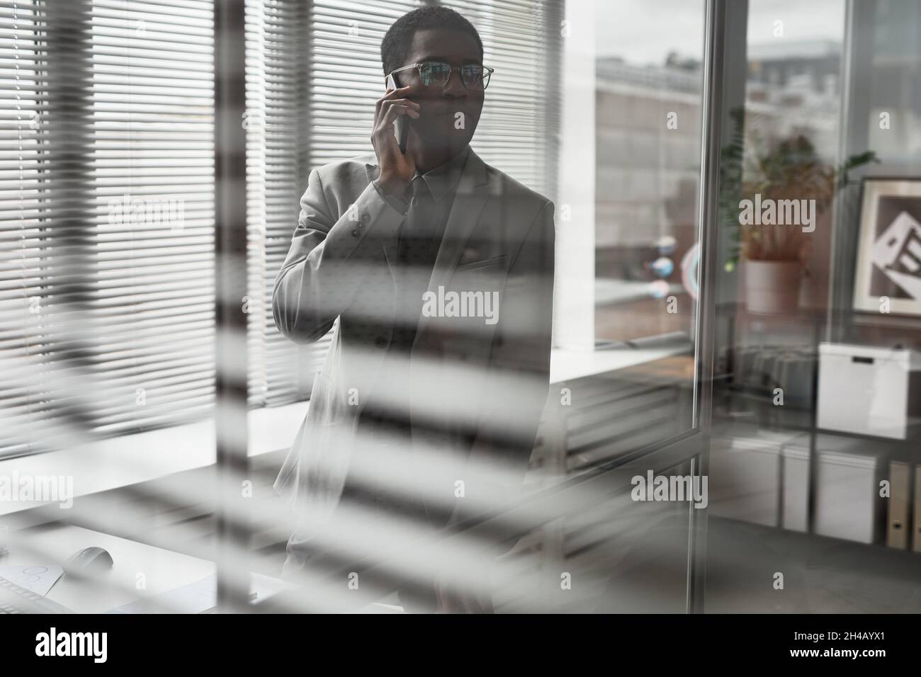 Waist up portrait of successful black businessman speaking by smartphone in office shot through glass, copy space Stock Photo