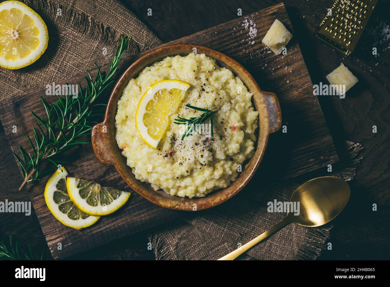 Lemon rice risotto with rosemary and fresh lemon slices on dark wooden background, top view Stock Photo