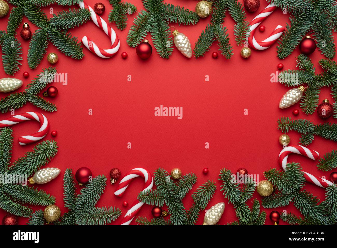 Red Christmas background with decorative frame made of fir branches and tree decorations. Flat lay, top view and copy space for text Stock Photo