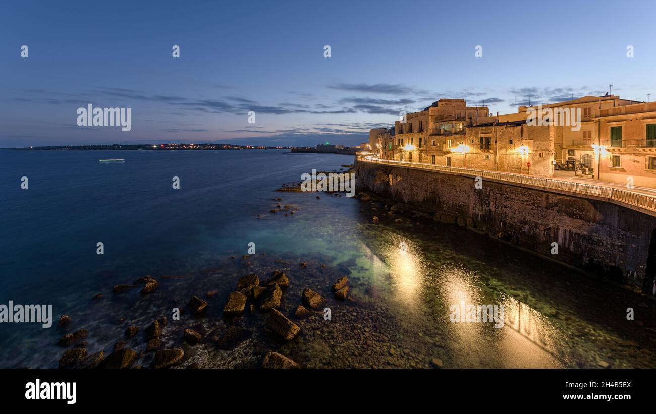 Sunset on the coast of Ortigia, a travel destination and an ancient Greek city in Syracuse, Sicily, Italy, with the old medieval town and the Mediterr Stock Photo