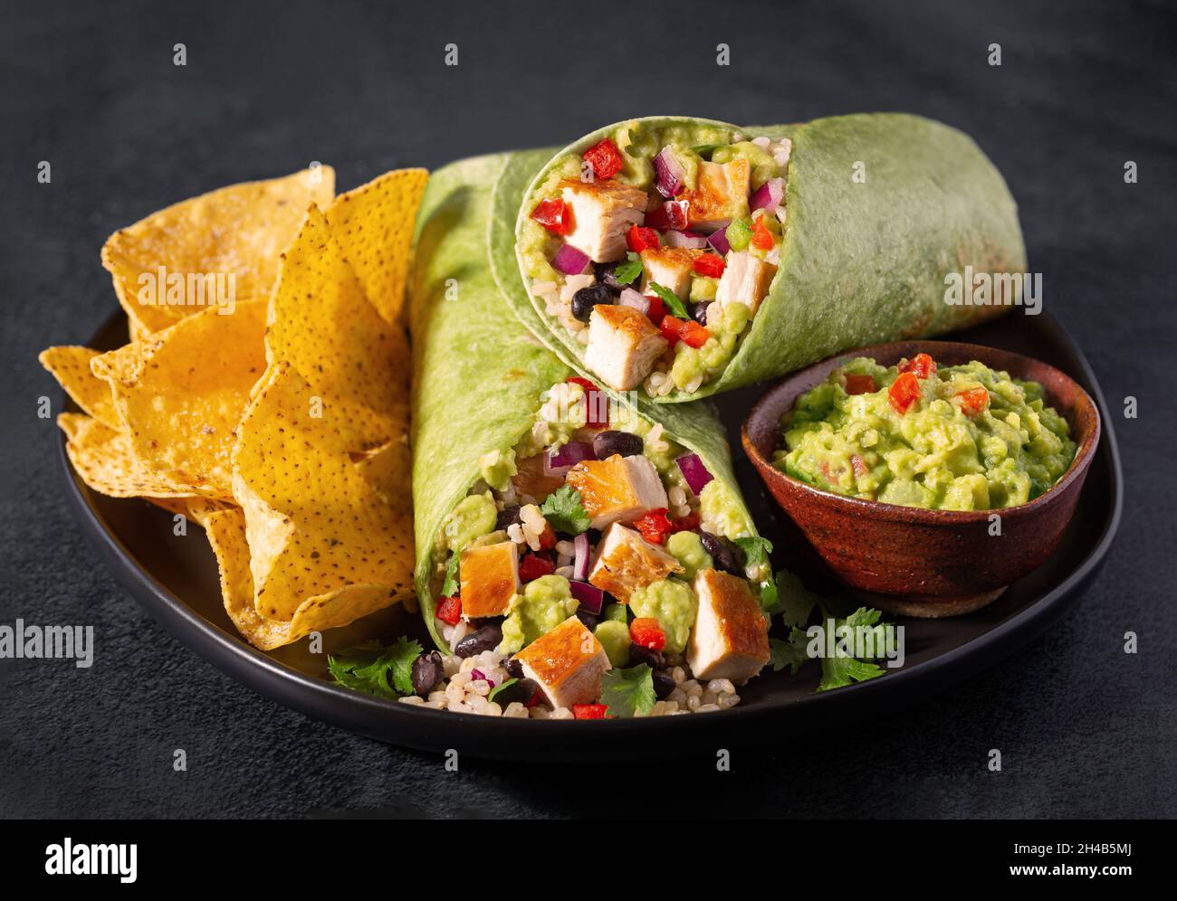 Chicken burrito in a spinach tortilla with corn chips and guacamole