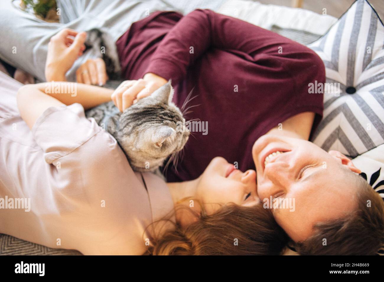 Lovely couple stroking cat lying on bed Stock Photo