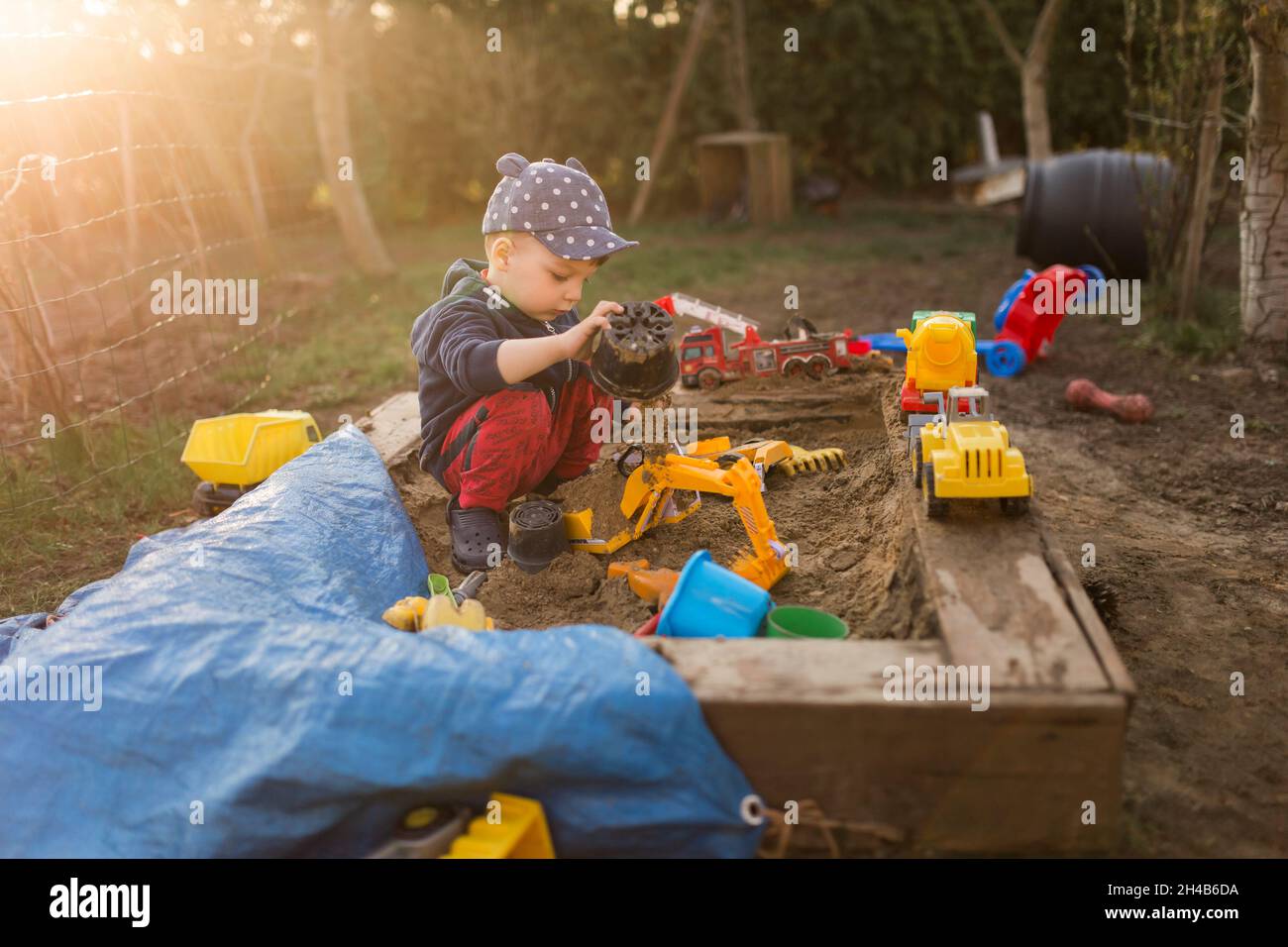 Small boy surrounded by toys squat in sandpit and playing with s Stock Photo