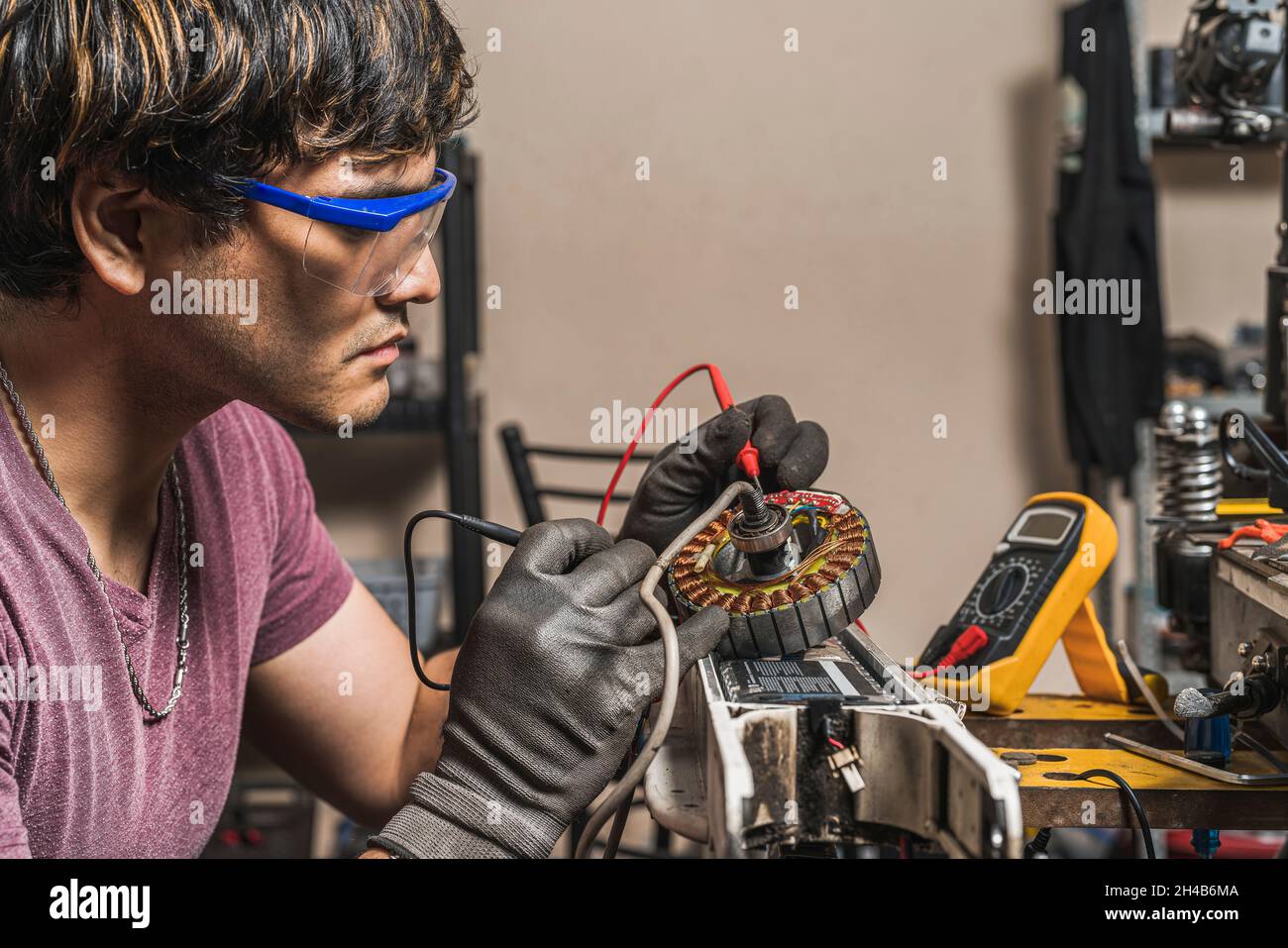 Side view of a specialist using a digital multimeter to check the correct voltage of an electric scooter in a specialist workshop. Stock Photo