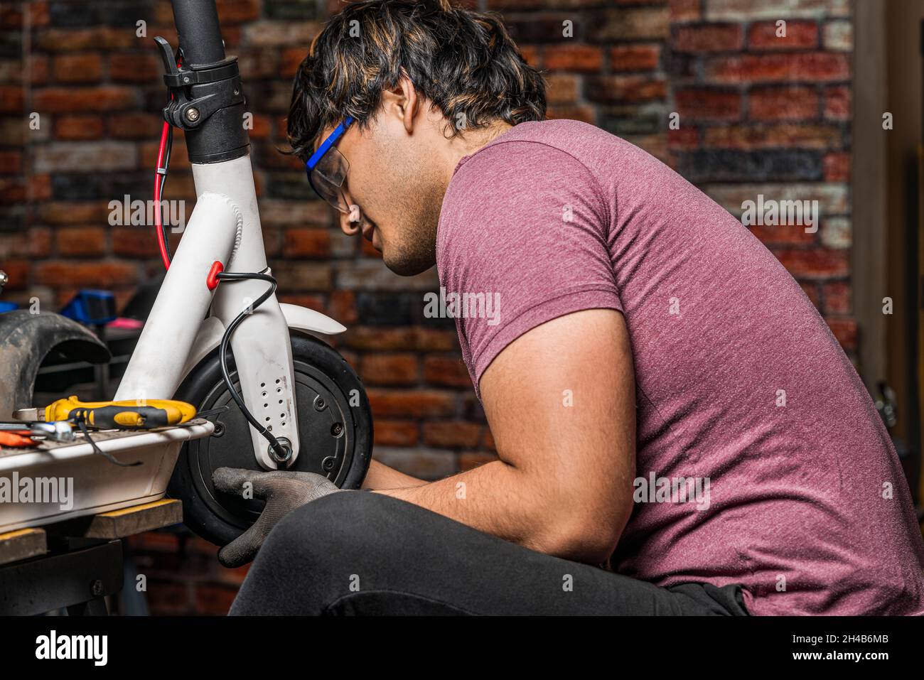 A seated latin mechanic puts a wheel of an electric scooter back in