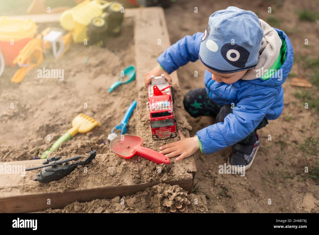 Small boy playing with toys in sandpit wearing blue clothes Stock Photo