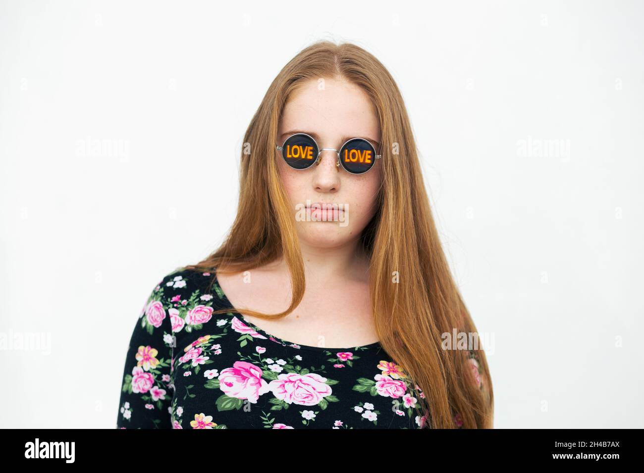 Redhead female teenage girl with long red hair in funny sunglasses  standing against the white wall Stock Photo