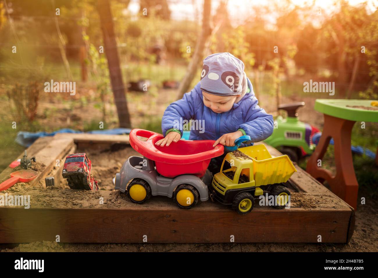 Small boy playing with toys in sandpit wearing blue clothes Stock Photo