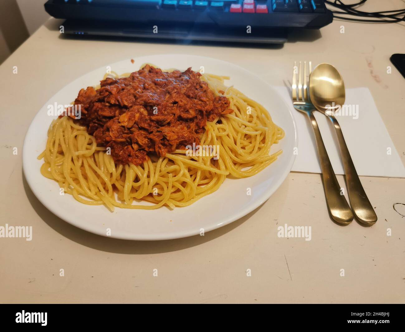 Spaghettis with a sauce on it in front of a laptop and silverware. Stock Photo