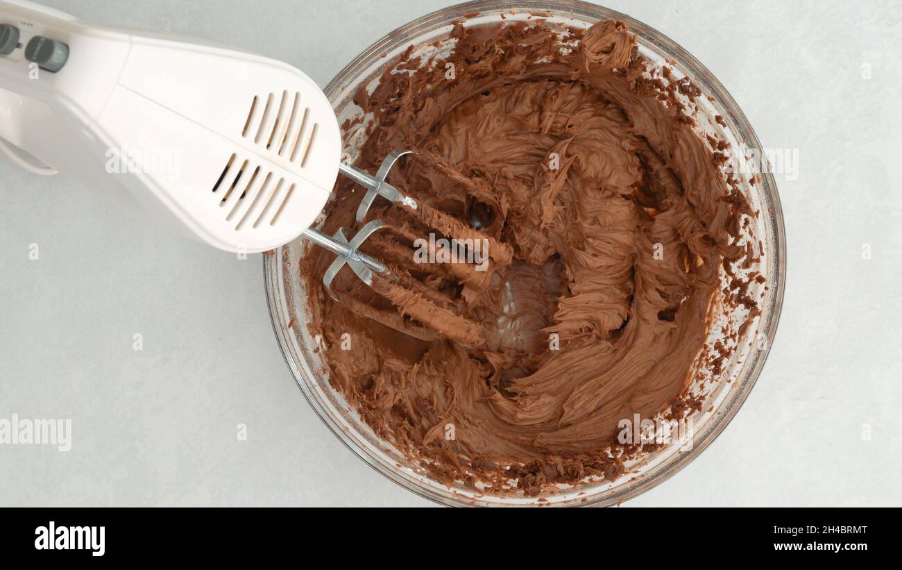 Chocolate icing in a glass bowl, mixing ingredients together using an