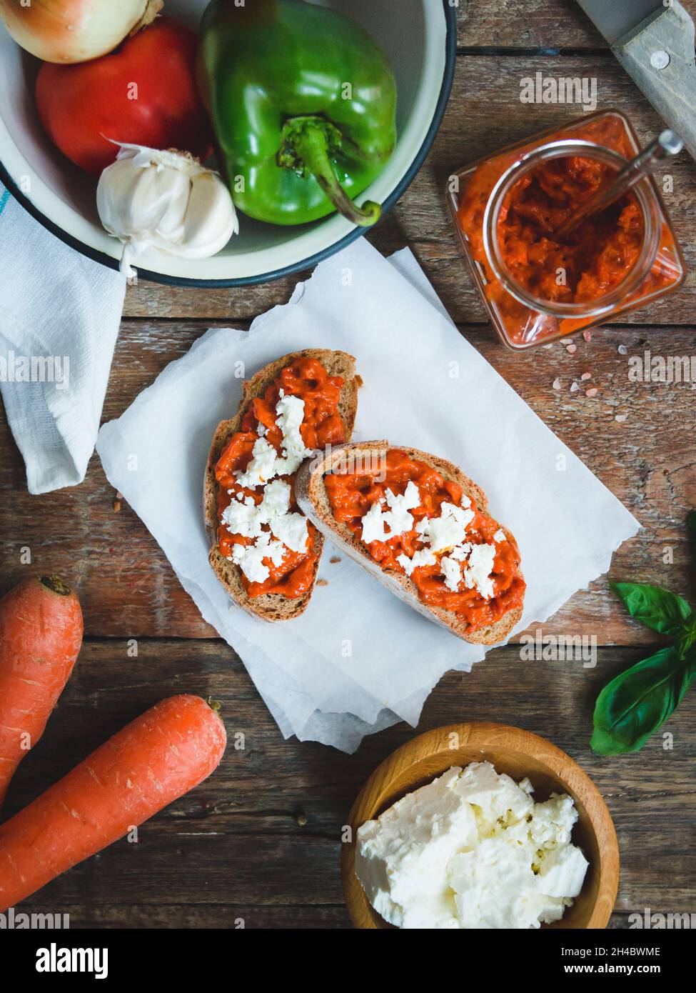 Wholegrain bread covered with tomato-pepper dip and feta cheese over old rustic wooden table. Homemade organic vegetable dish. Stock Photo