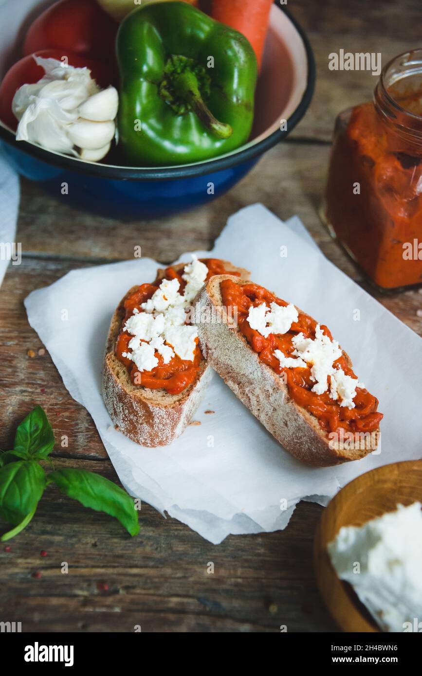 Wholegrain bread covered with tomato-pepper dip and feta cheese over old rustic wooden table. Homemade organic vegetable dish. Stock Photo