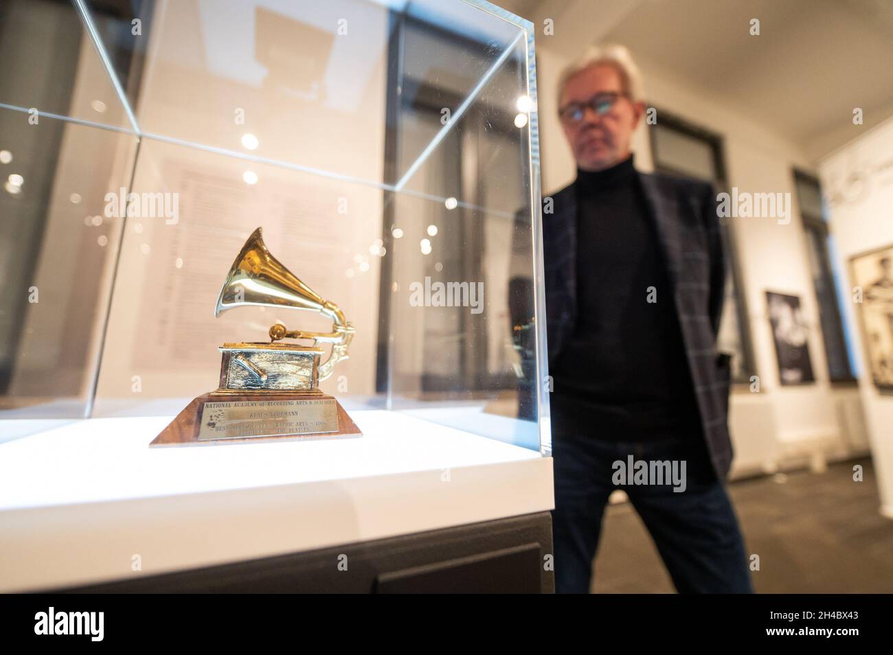 11 October 2021, Lower Saxony, Lüneburg: Carsten Junge, director of the Kunsthalle der Sparkassenstiftung Lüneburg, is standing next to a golden Grammy, which Klaus Voormann received for the Best Album Cover. Klaus Voormann is considered the fifth Beatle, he met the Beatles in 1960 in the Kaiserkeller on St. Pauli. In the Kultur Bäckerei Lüneburg an exhibition is dedicated to his life's work for the first time. (to dpa 'Klaus Voormann - no one was as close to the Beatles') Photo: Philipp Schulze/dpa Stock Photo