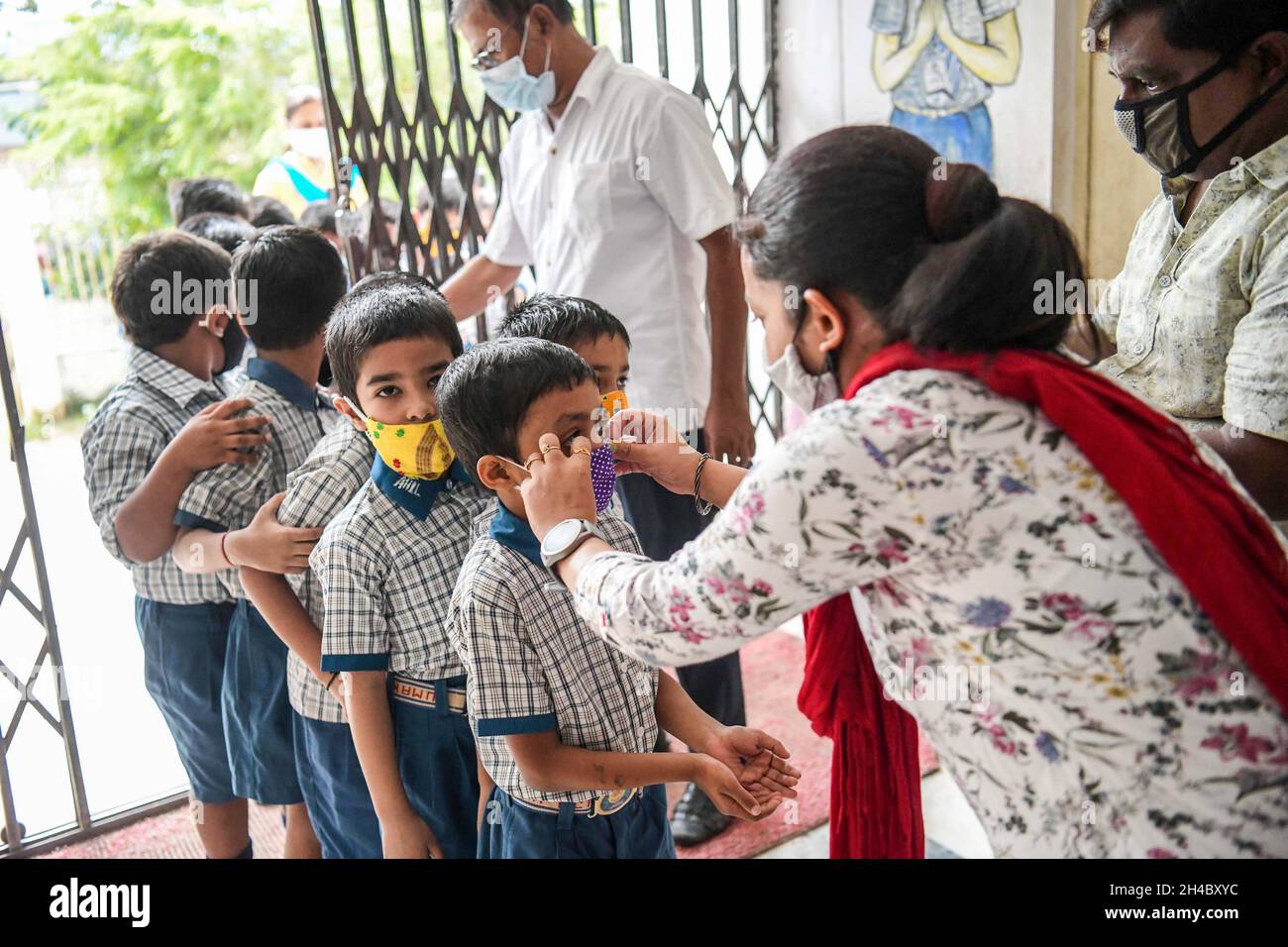 Teachers helping children to put on masks before entering the classroom on the first day of reopening of the nursery sections at schools. Agartala, Tripura, India. Stock Photo