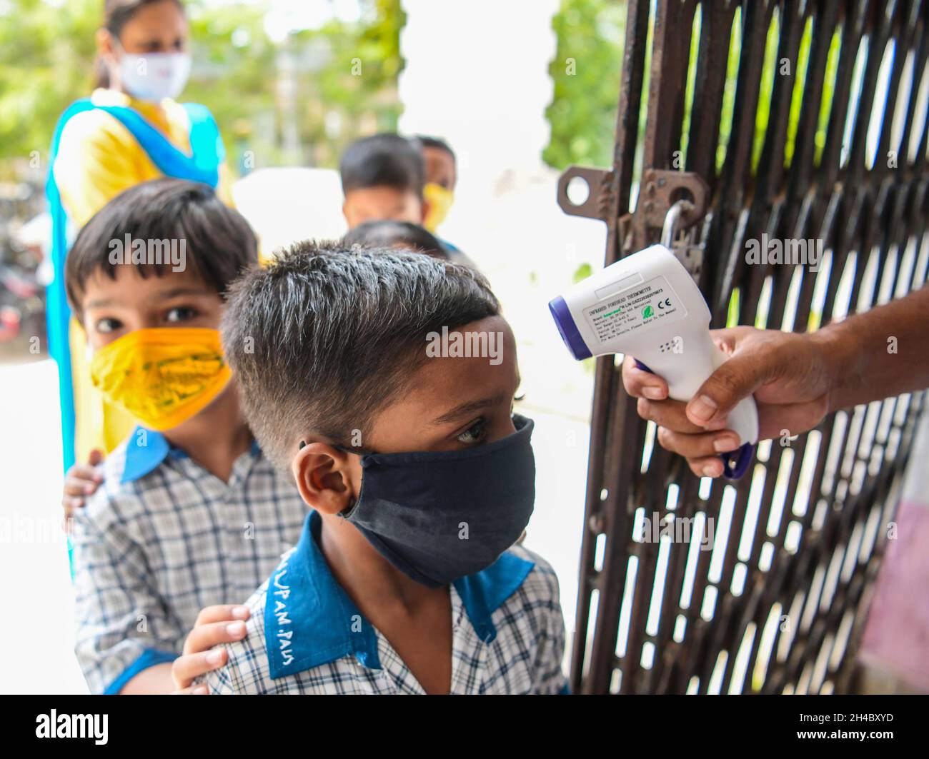 Teachers helping children to put on masks before entering the classroom on the first day of reopening of the nursery sections at schools. Agartala, Tripura, India. Stock Photo