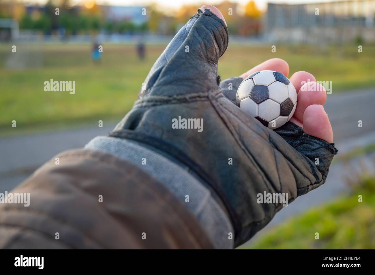 a small decorative ball, a symbol of football, in the outstretched hand of a man in a leather glove against the background of a football field Stock Photo