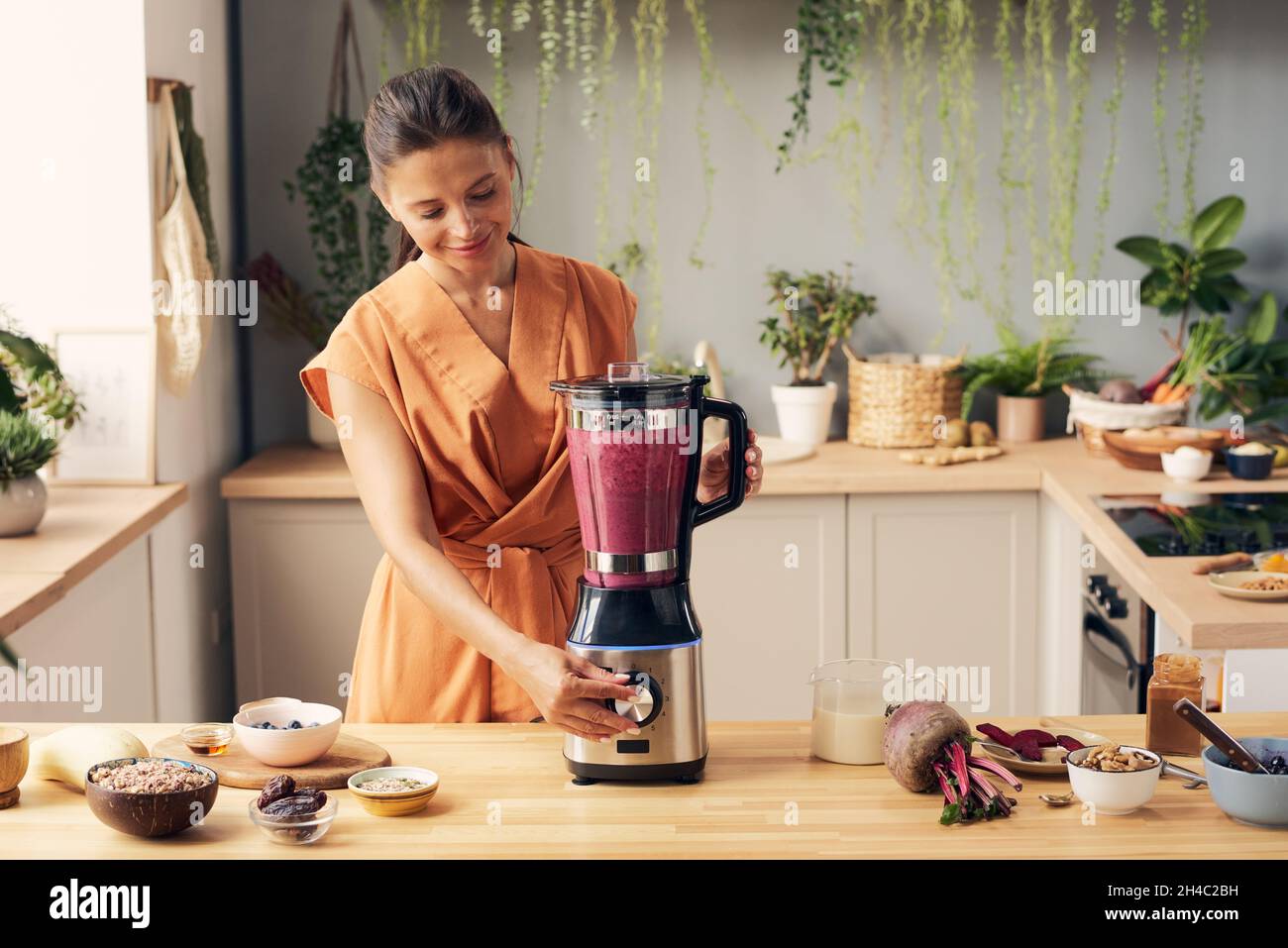 Young female pressing start button of blender during preparation of
