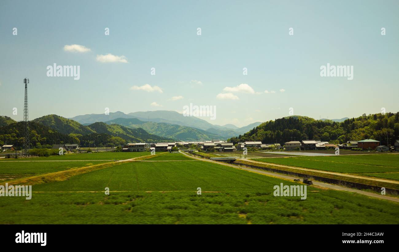 Panoramic view of a meadow and village houses of rural area in Japan with mountains and blue sky background. No people. Stock Photo