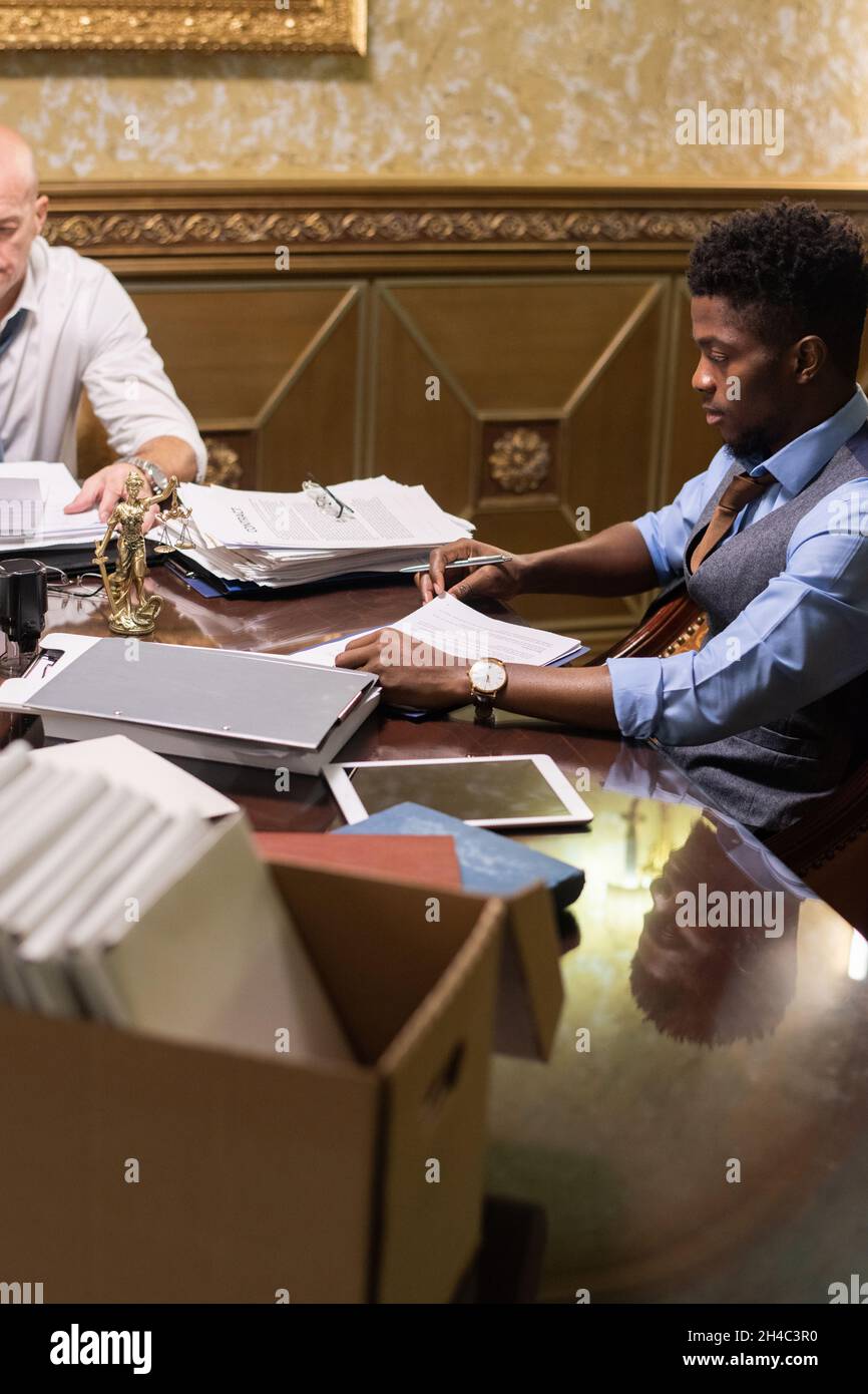 Young African man and his mature colleague in formalwear working with business contracts and other documents in boardroom Stock Photo