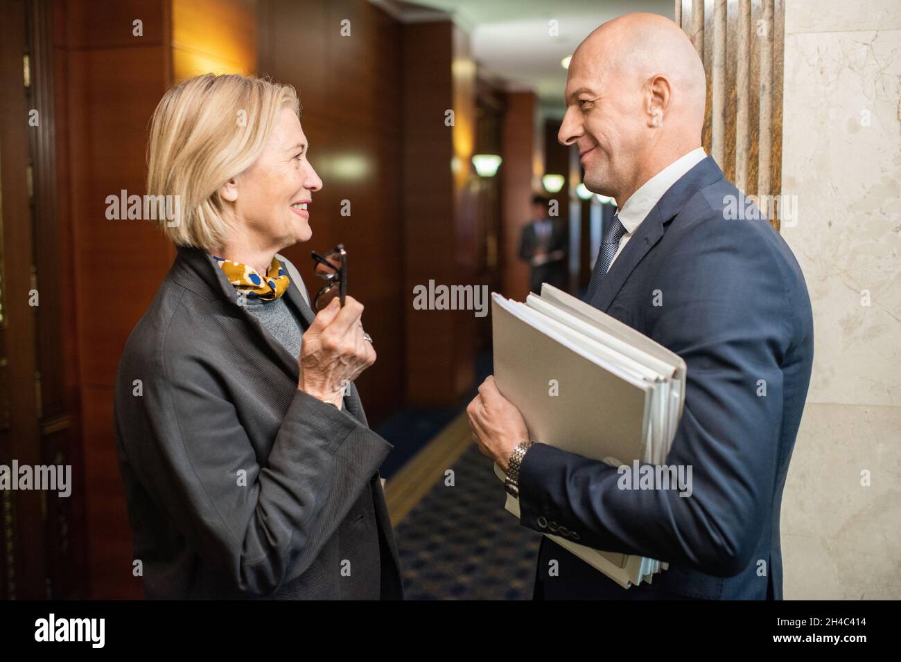 Two elegant mature colleagues discussing news or working points while standing in corridor of contemporary office center Stock Photo